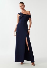 Granatowa suknia wieczorowa z odkrytymi ramionami, ozdobnym topem, dopasowanym krojem, rozcięciem do uda oraz gładkim materiałem.