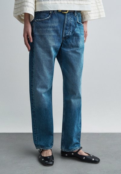 Lyseblå straight-leg jeans i denim med en let falmet finish. Kombineret med sorte flade sko med sølvdekorationer.