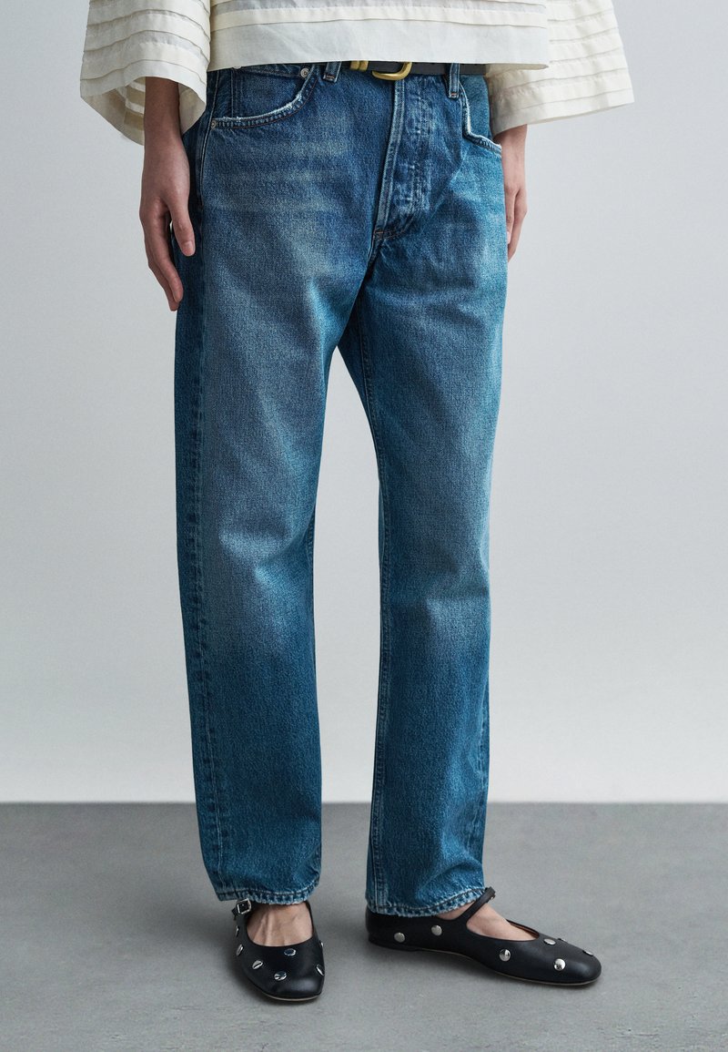 Svetlomodré rifle rovného strihu s jemne vyblednutým efektom. Kombinované s čiernymi plochými topánkami so striebornými ozdobami.