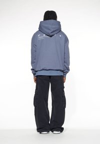 Hoodie i mjuk, texturerad mörkblå tyg med vita grafiska detaljer på baksidan. Kombination med löst sittande svarta cargo-byxor.