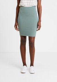 Jupe crayon vert menthe en matière extensible. Design taille haute avec une texture lisse, assortie à des baskets blanches.