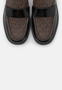 Mocassins en tissu marron présentant un motif géométrique, des accents en cuir verni noir, une forme classique de mocassin, et une semelle en caoutchouc robuste.