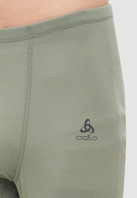 Primo piano di un tessuto verde oliva senza cuciture con cuciture verticali e logo Odlo nero nella zona dell'anca di abbigliamento aderente.