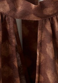 Tissu marron avec des plis froncés et un détail d'une fente verticale en gros plan.