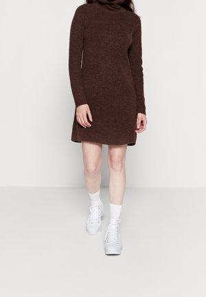 Abito turtleneck in maglia marrone con maniche lunghe, texture a coste e spacchi laterali, abbinato a scarpe da ginnastica bianche e calzini alla caviglia.