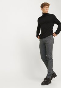 Schwarzer Rollkragenpullover mit langen Ärmeln, kombiniert mit grauen Nadelstreifenhosen. Die Schuhe sind dunkelbraun mit Schnürsenkeln und einer strukturierten Oberfläche.