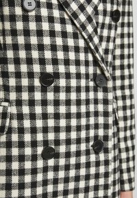 Double-breasted blazer in een zwart-wit geruit patroon, met gestructureerde stof en ronde zwarte knopen, voorzien van twee klepzakken.