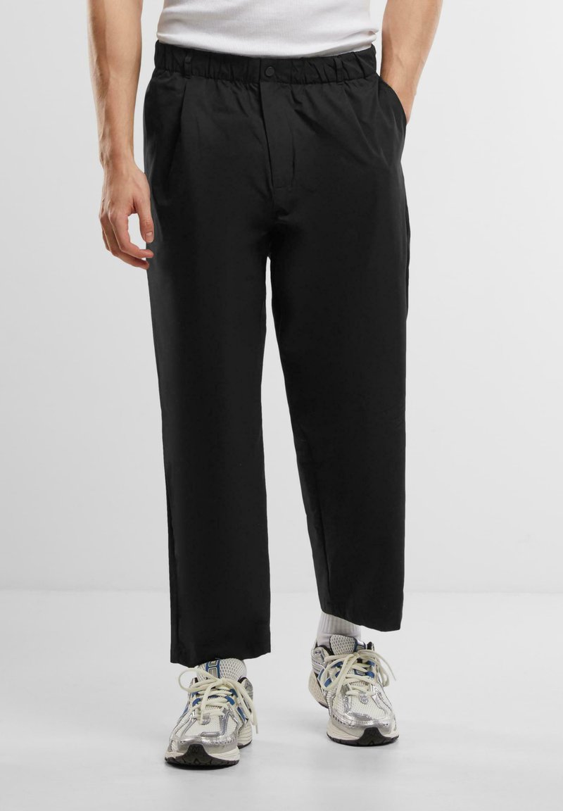 Pantaloni negri cu o croială lejeră, dotati cu un talie elastică și pliseuri frontale. Purtați cu adidași texturați, multicolori.