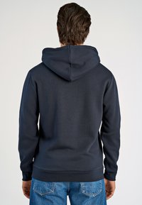 Felpa blu navy con cappuccio, realizzata in tessuto morbido, con schiena senza cuciture e polsini a coste. Cuciture piatte distintive.