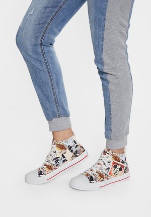 Nogi ubrane w dwukolorowe niebiesko-szare spodnie dresowe i wysokie sneakersy z kolorowym wzorem z komiksu Mickey Mouse.