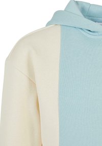 Felpa con cappuccio nei colori crema e azzurro chiaro, caratterizzata da un tessuto testurizzato con un design a blocchi di colore distintivo sulla parte anteriore.