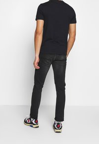 Camiseta negra de manga corta, combinada con jeans oscuros y zapatillas coloridas que presentan patrones y colores variados sobre un fondo blanco.