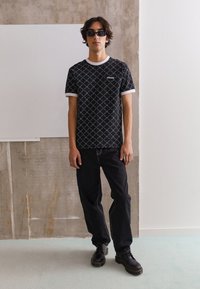 Black patterned t-shirt with white trim, featuring a grid design and logo. Paired with dark jeans and black lace-up boots.