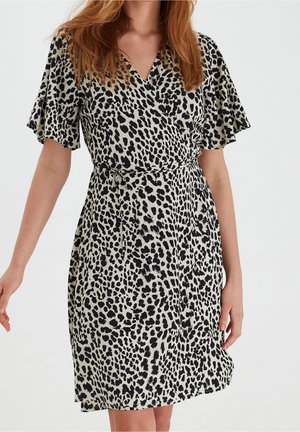 Femme portant une robe à manches courtes, longueur genoux, avec un motif léopard noir et blanc et une ceinture nouée à la taille.