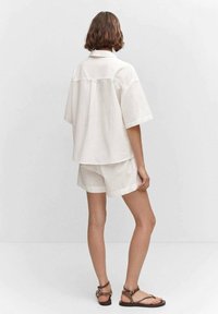 Chemise à manches courtes ample de couleur claire assortie à un short du même ton. Le tissu semble doux, avec un design décontracté et des coutures minimalistes.