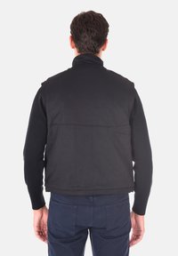 Gilet nero con zip e un motivo testurizzato, caratterizzato da un alto colletto e un design senza cuciture, indossato sopra una maglietta a maniche lunghe e pantaloni blu navy.