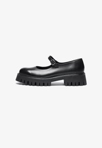 Black leather Mary Jane-style shoe with a round toe, ankle strap, and chunky rubber sole featuring ridged detailing.