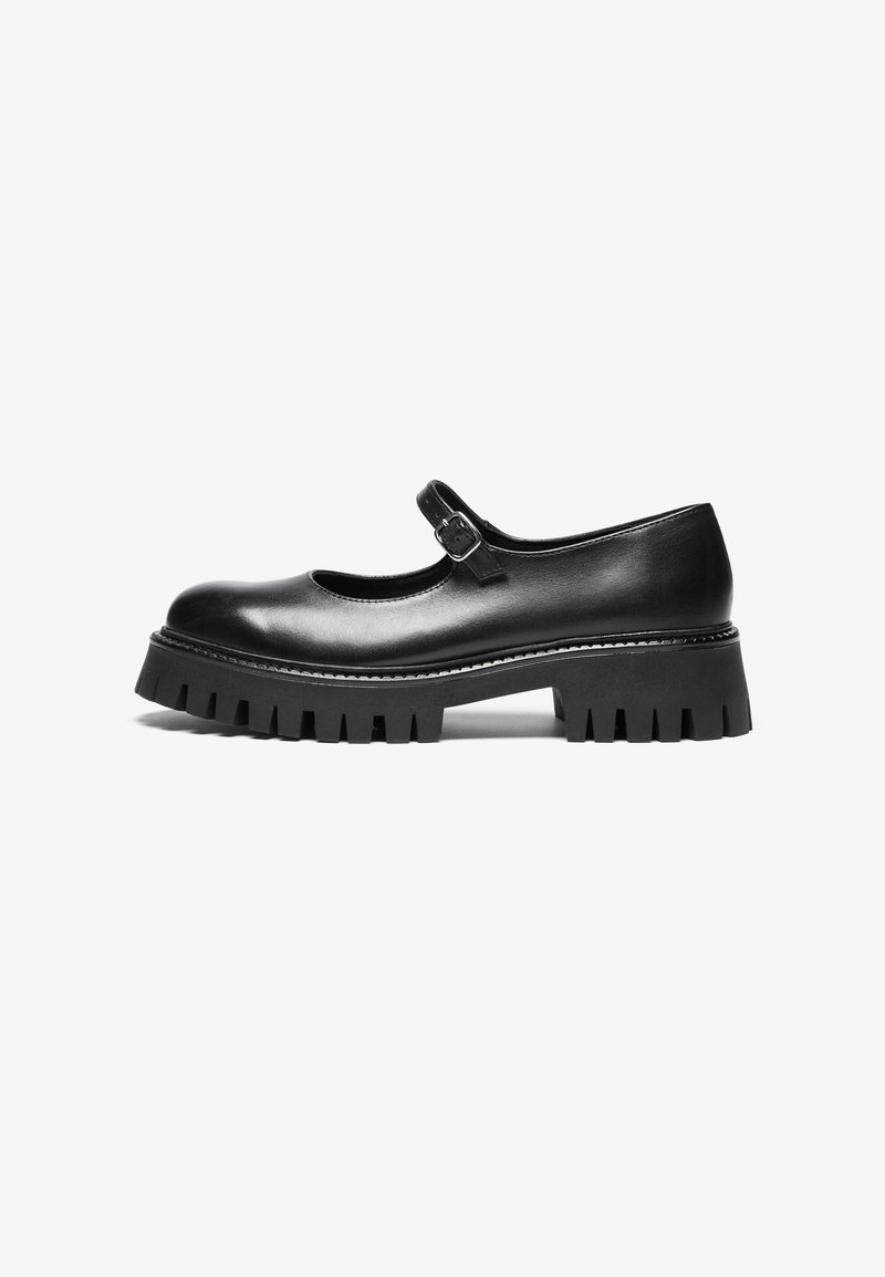 Black leather Mary Jane-style shoe with a round toe, ankle strap, and chunky rubber sole featuring ridged detailing.