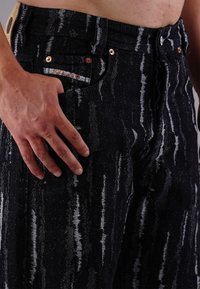 Black denim jeans with a textured, striped pattern. Features copper hardware, a stitched label on the waistband, and front pockets.