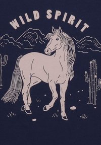 Marineblauer Stoff mit einer hellrosa Grafik, die ein Pferd zwischen Kakteen und Bergen darstellt, mit dem Text "WILD SPIRIT" darüber in einer geschwungenen Schriftart.