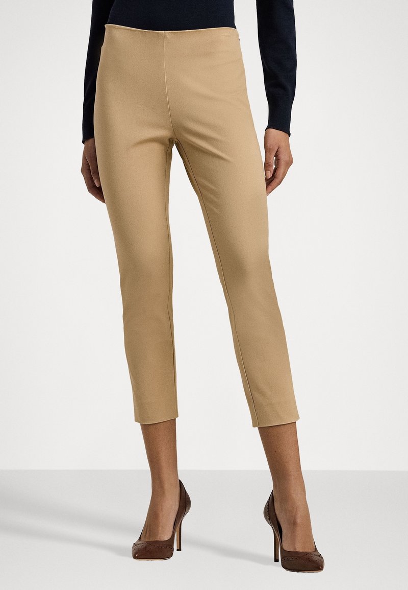 Pantalons stretch beiges avec une silhouette ajustée, longueur mi-mollet et texture lisse, associés à des talons hauts marron.