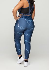Leggings azul marino con un estampado floral, diseño de cintura alta y tejido elástico, combinados con un sujetador deportivo de malla negra y zapatillas blancas.