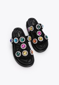 Sandali neri con texture trapuntata, numerosi grandi gemme colorate incastonate in cerchi argentati, dotati di cinturini regolabili per una vestibilità perfetta.