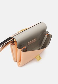 Brzoskwiniowa skórzana torebka z złotym zapięciem otwarta, ukazująca jasnoszare wnętrze, metkę i dwie przegródki na białym tle.