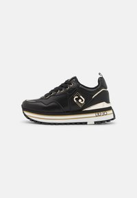 Sneaker nera con tomaia in pelle liscia e dettagli dorati. Presenta una suola intermedia bianca spessa con strisce dorate e una suola in gomma testurizzata.