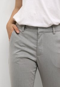 Harmaat housut, jotka on valmistettu sileästä kankaasta. Niissä on suora etuosa, sivutaskut ja istuva malli. Yhdistetty valkoiseen yläosaan.