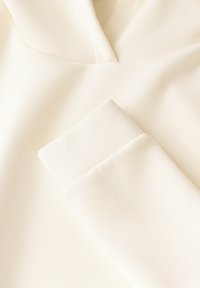 Felpa color crema con una texture morbida e liscia. Presenta un cappuccio arrotondato e maniche con polsini, con dettagli di cucitura sottili.
