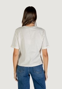 T-shirt beige chiaro a maniche corte con collo rotondo e vestibilità rilassata. Materiale in cotone, texture liscia. Indossato con jeans di denim blu.