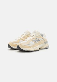 Sneakers atletici beige e bianchi con texture in rete e suede, con accenti grigi, una suola ammortizzata e un branding prominente sul lato.