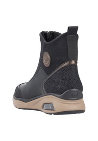 Botte noire à la cheville avec caoutchouc noir texturé, une tige en cuir lisse, des accents en bronze et une fermeture éclair. Comprend une semelle beige rembourrée.