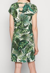 Krátké šaty bílé barvy s velkým potiskem zelených tropických listů. Zadní strana má výřez a přiléhavý siluetu.