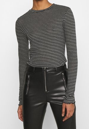 Osoba ubrana w długi rękaw szaro-czarną koszulę w poziome paski, wpuszczoną do wysokowtalowych czarnych skórzanych spodni z przednimi kieszeniami na zamek.