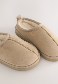 Chaussons beiges en daim doux, dotés d'une doublure en polaire, d'un col élastiqué et d'un détail cousu le long de la couture avant.