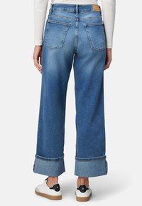 Dżinsy z szerokimi nogawkami w kolorze niebieskim z surowym wykończeniem, dwoma tylnymi kieszeniami i podwinięciem na kostce. Połączone z białymi trampkami z czarnymi akcentami.