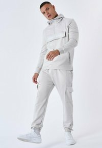 Lichtgrijze trainingsoutfit bestaande uit een hoodie met een voorzak en logo, gecombineerd met cargobroeken, gemaakt van een soepele, rekbare stof.