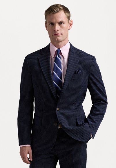 Completo navy a righe sottili con un design aderente, abbinato a una camicia rosa chiaro e una cravatta blu a righe. Include un fazzoletto da taschino.