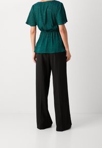 Blusa teal con maniche corte e vita elasticizzata, abbinata a pantaloni ampi neri. Tessuto morbido con un sottile motivo floreale.