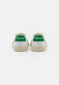 Sneakers bianchi in tela con accenti verdi sul tallone e sul logo. Punta rotonda, superficie texturizzata e suola in gomma beige per la trazione.