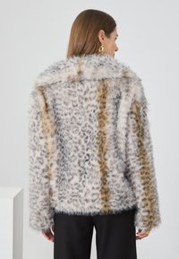 Chaqueta de piel sintética con un patrón de manchas en gris y beige, que presenta un amplio cuello y mangas largas. Acabado texturizado y suave.