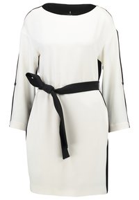 Robe blanche avec des accents noirs, présentant un décolleté bateau, des manches trois-quarts et une ceinture nouée à la taille. Tissu lisse avec des panneaux latéraux.