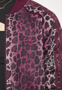 Fialová a černá bunda s leopardím potiskem, žebrovaným límcem, bočními pruhy a vyšívaným logem na hrudi. Hladká textura.