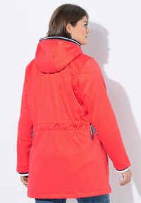 Rode softshell jas met een capuchon, trekkoord in de taille en contrasterende marineblauwe accenten op de kraag. Glad textuur en een ontspannen pasvorm.