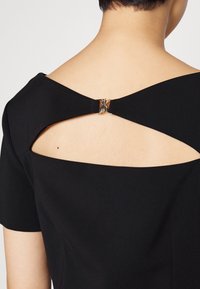 Vestido negro con mangas cortas y espalda con corte acentuada por un cierre metálico. Textura suave y diseño ajustado.