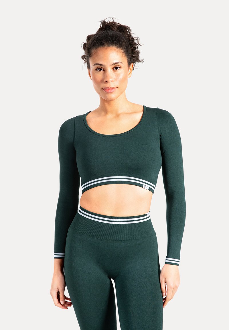 Donkergroene cropped top met lange mouwen, een gebogen halslijn en horizontale witte strepen bij de zoom, gecombineerd met bijpassende hoge taille legging.