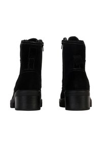 Black ankle boots made of suede with a smooth finish, featuring a low block heel, side zippers, and contrasting white stitching details.