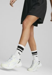 Baskets de sport blanches avec des accents argentés, associées à des chaussettes blanches arrivee avec des rayures noires et un logo noir, portées avec une robe noire.